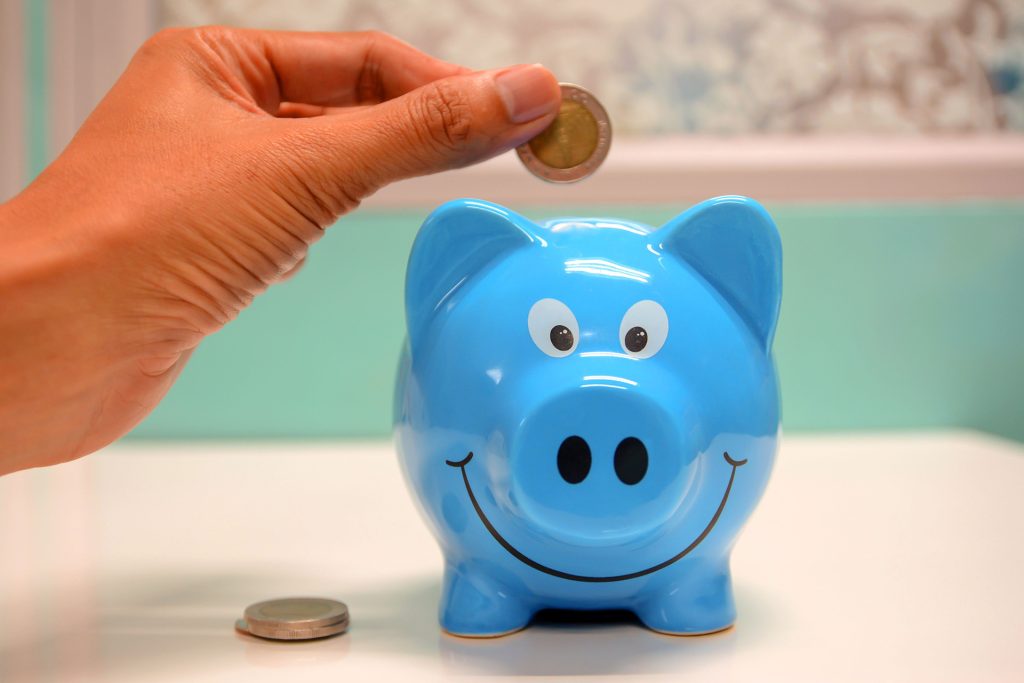 hand placing coin into blue piggy bank